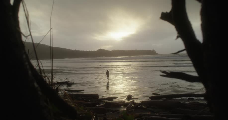 A lone person walks down the beach during a sunset rainstorm