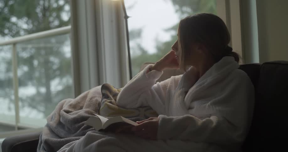 Woman in a robe enjoying early morning weather while holding a book