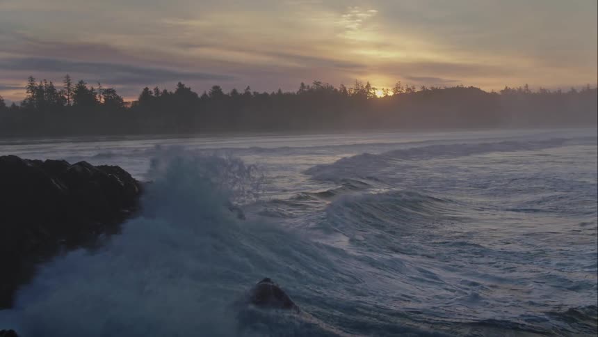 Aerial view of the sun rising over the mountains and crashing ocean waves