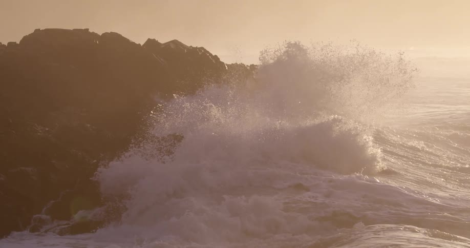 Waves splash against rocky coastline as morning sun shines bright