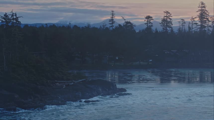 Sea fog reveals cabins on rocky ocean beach and distant mountains