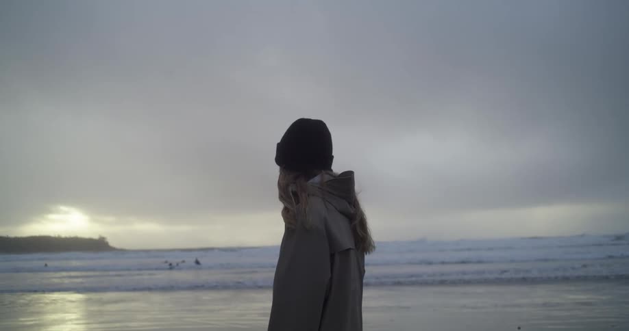 Woman standing on a shore looking out at the ocean while the sun sets