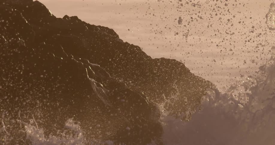 Waves crashing in to rocks on the shore against sun