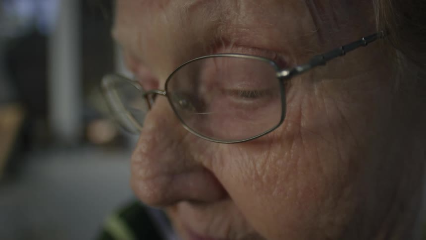 An elderly woman wearing glasses blinks