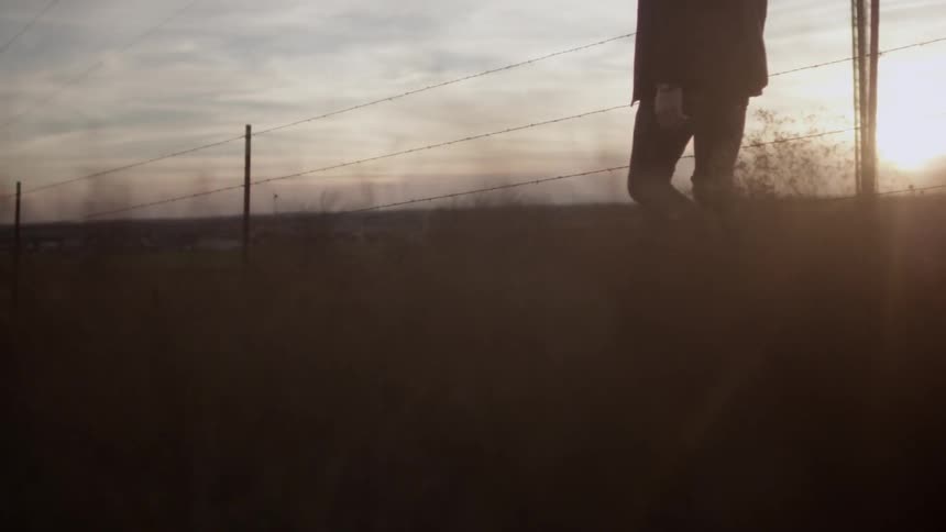 Man walking in a field next to a barbed wire fence
