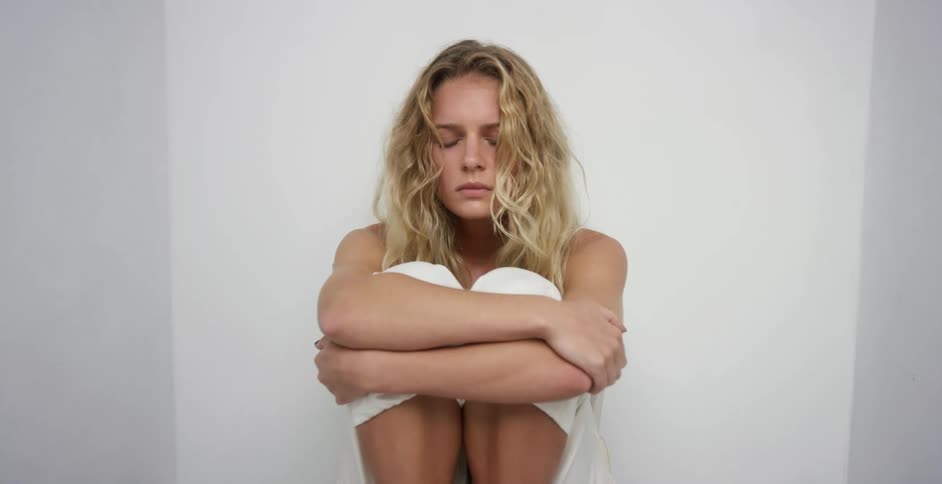 A young woman sitting in a fetal position in small white room