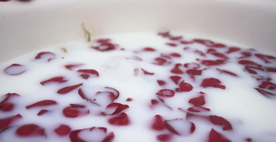 Woman submerges her head under water in a bathtub full of foggy white water and red rose petals