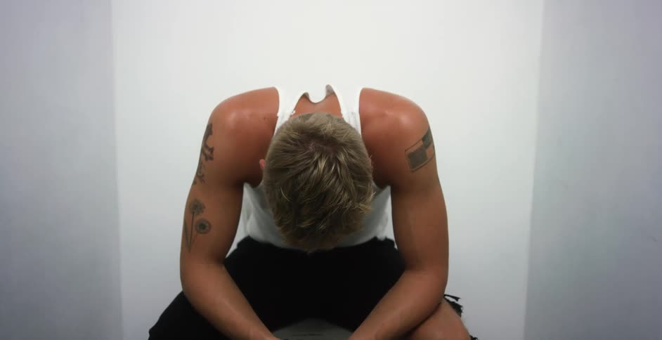 White tattooed man sitting alone in an empty room with his head down