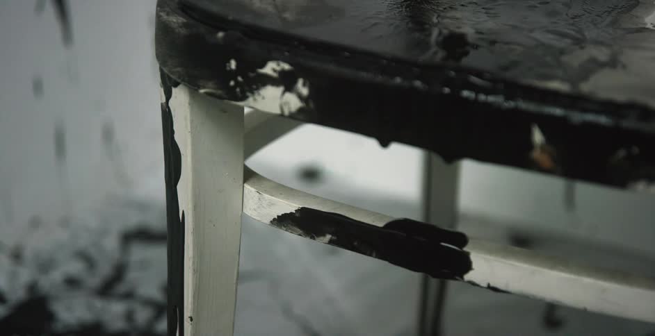 Bright black ink spilled over a white chair in a white room
