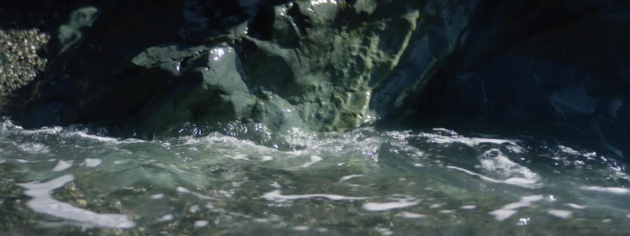 Water flows up towards a rocky shoreline and then recedes swiftly