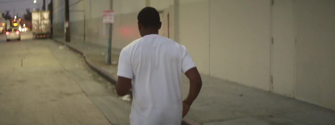 Man jogs down a street in an urban area at night while car drives by on the left