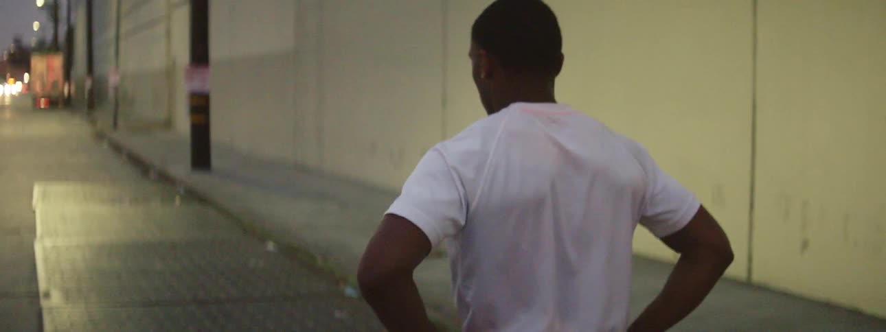 A man walks down a city street and then stretches his arm in front of him