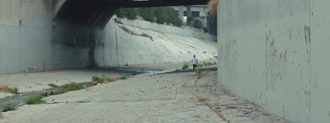 A man running in a ditch under a street