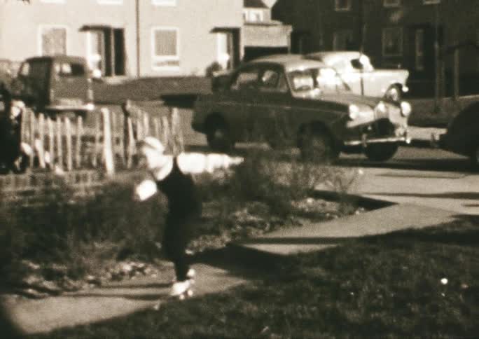 Young girl tries to keep her balance while roller skating on a sidewalk as cars sit parked on the street