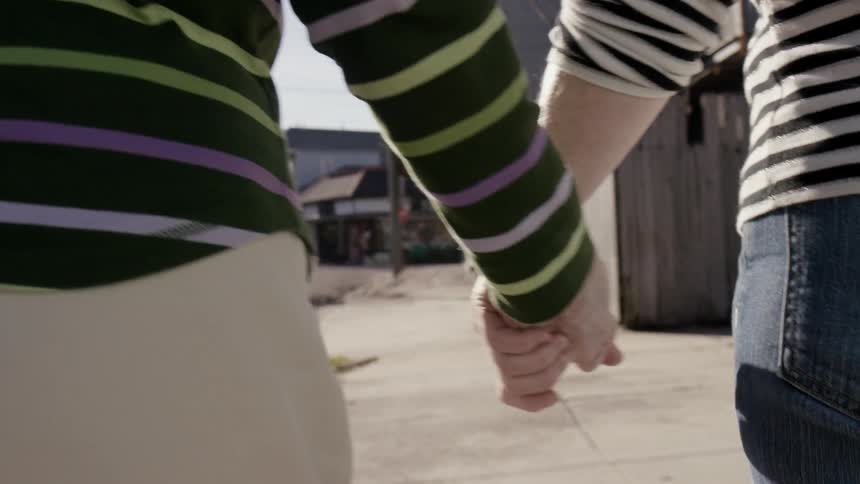 Two people hold hands while walking down the sidewalk