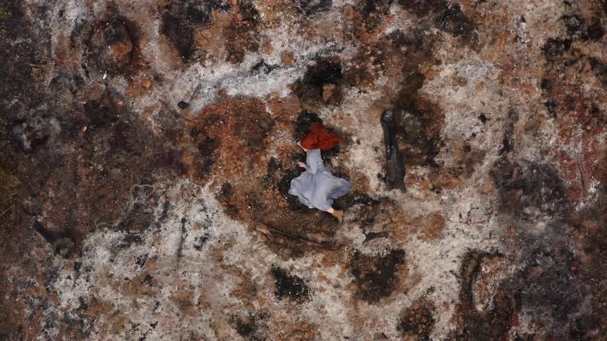 Twisting aerial view of a young long haired redhead woman in a blue dress laying in the floor over the moss and rocks