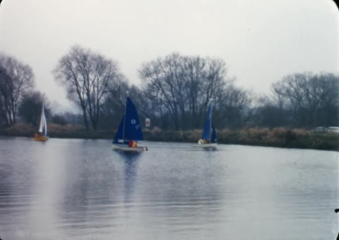 A lake with four sailboats with trees the sky and clouds in the background
