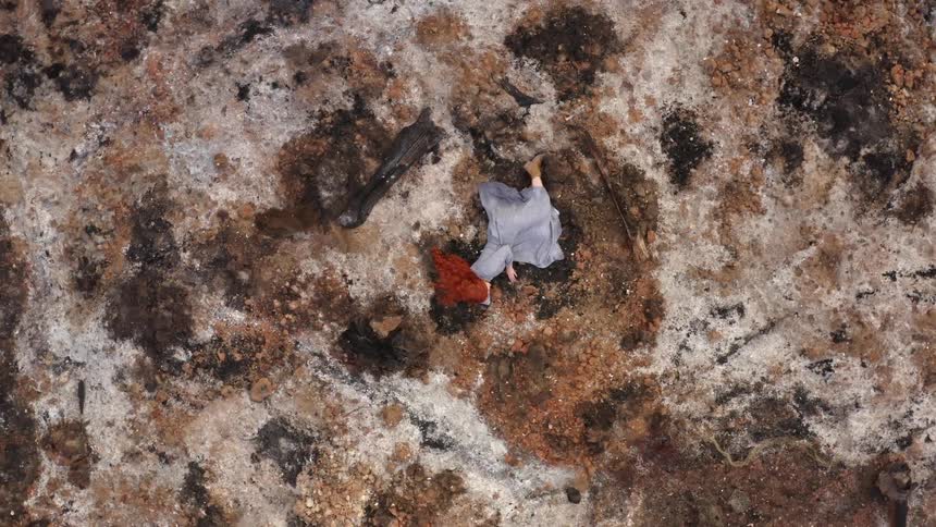A woman lying lifelessly on a ground of rocks