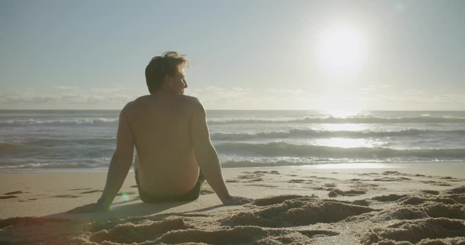 White man sitting at the beach alone next to the sea