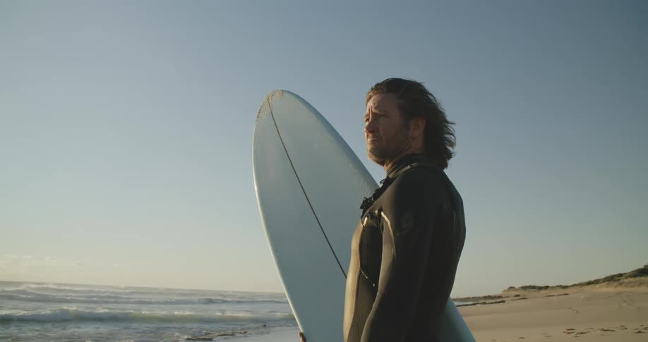 A man stands on a beach holding a surfboard