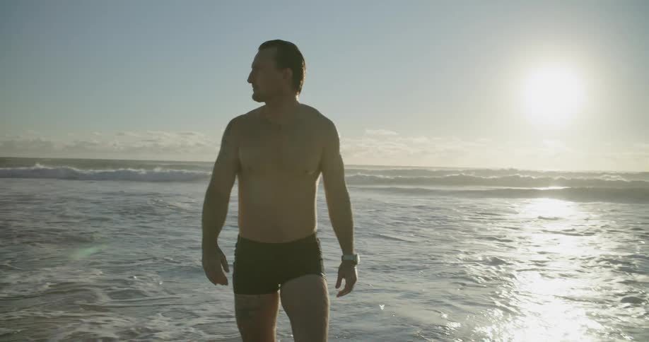 White man walking out of the sea while wearing swimming trunk
