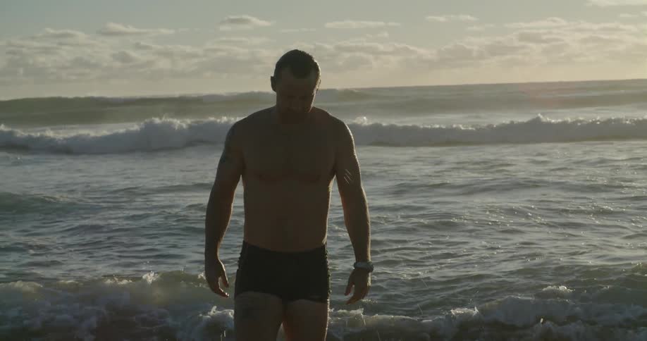 Man wearing swim trunks wades out of ocean