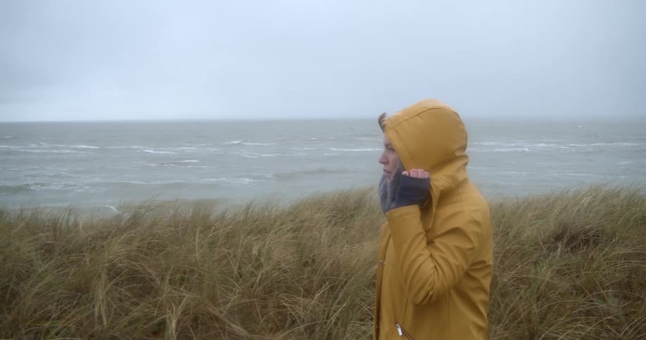 Woman wearing coat walks through grass on sea shore