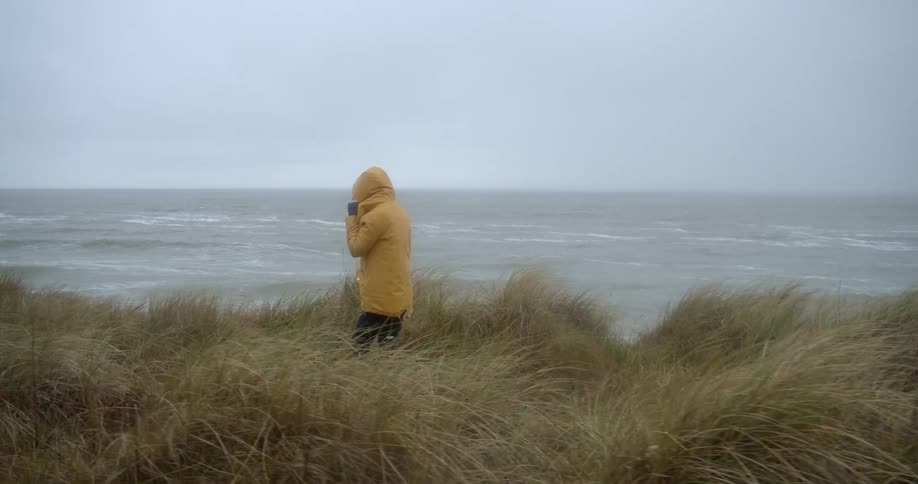 A person wearing a bright yellow raincoat windbreaker walking near the ocean