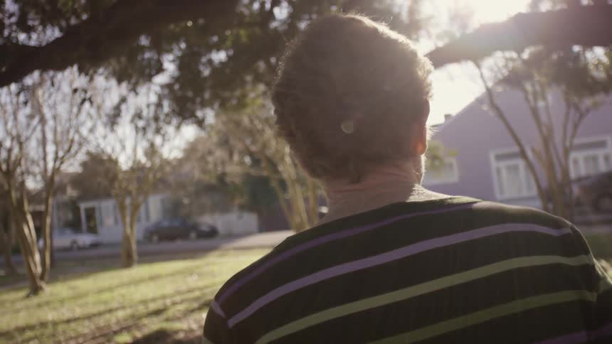 An older woman in a striped shirt walks on leaves