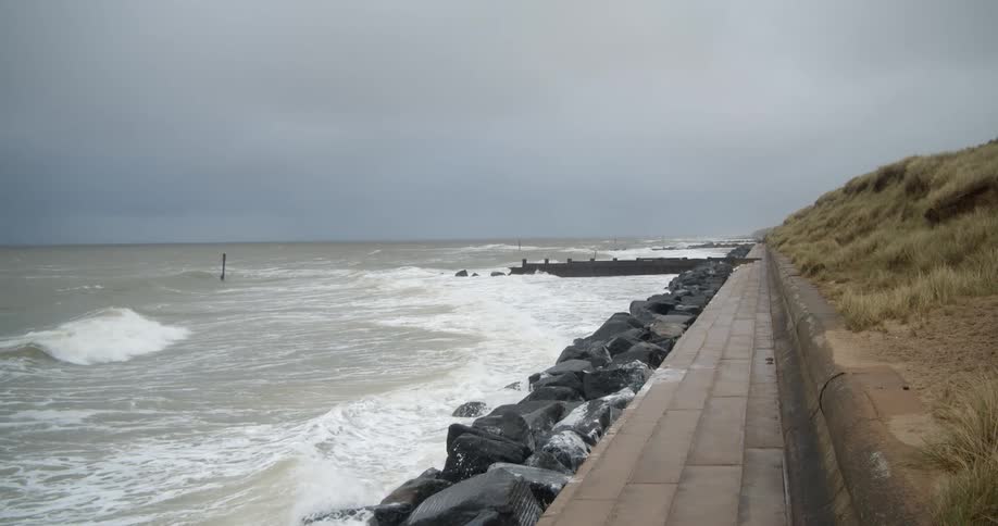 Waves from an ocean tide move towards rocks stacked next to a walkway at daytime