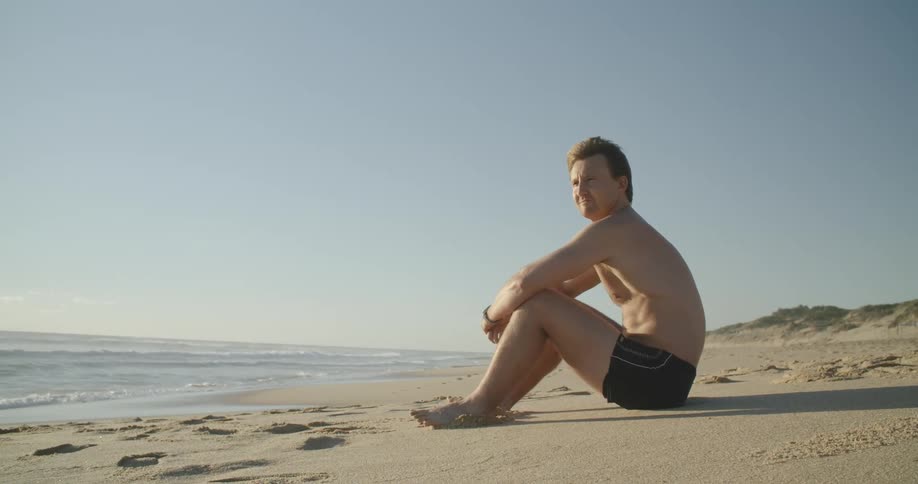 A man sitting on a sandy shoreline watching the ocean
