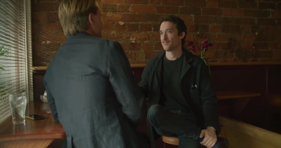 Two white men in a bar drinking cocktails and talking and laughing together
