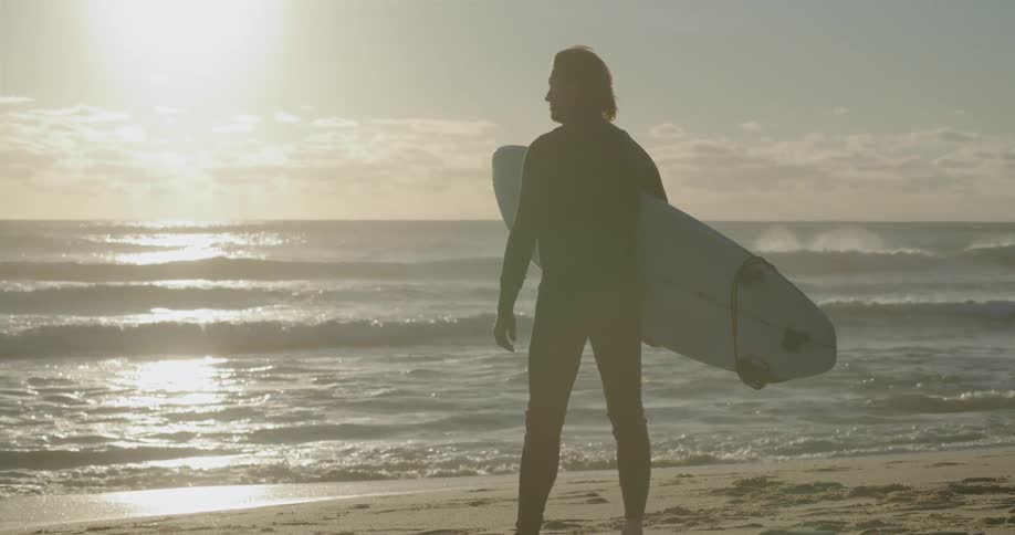 Man holding a surfboard next to the sea at the beach