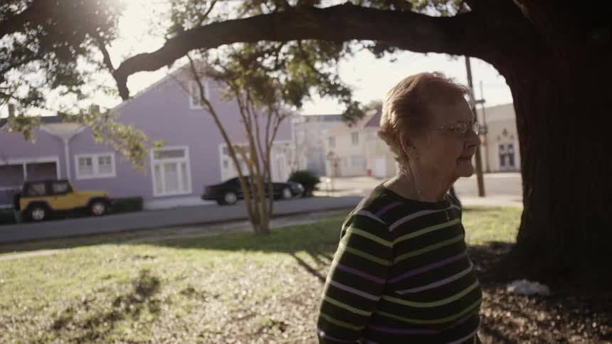 Older woman standing near a large tree in a neighborhood park
