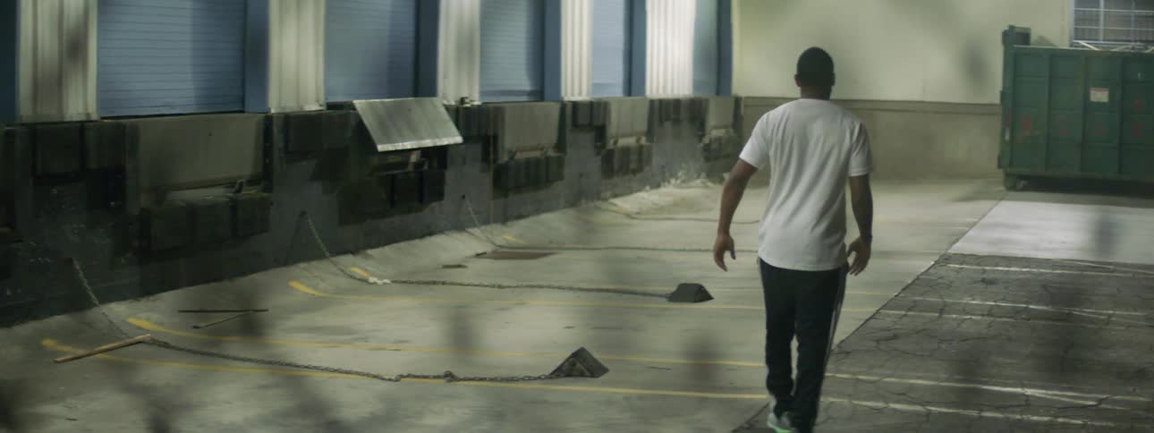 A man walks along the edge of a long loading dock and occasionally pauses to stretch his legs