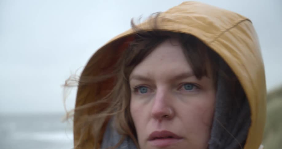 A woman walks along the coast with her hat pulled up
