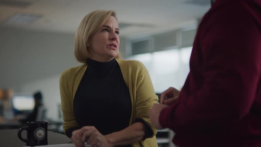 White woman holding a cup and a spreadsheet talking to a man that was writing down on a table