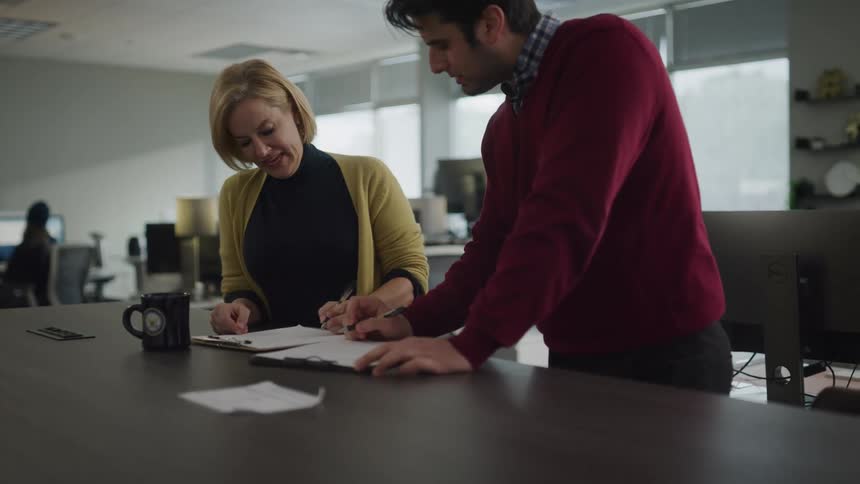 Man and woman laugh as they stand at a table in an office and draw with their pens on a paper