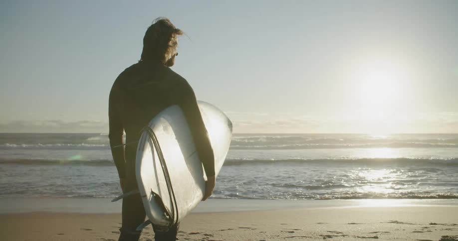 Man holding his surfboard while looking to the sea at the beach