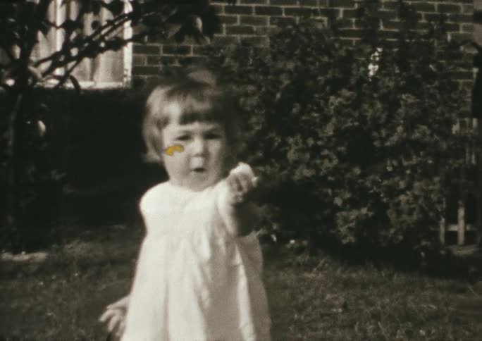 Vintage footage of a toddler walking and holding food outside a house