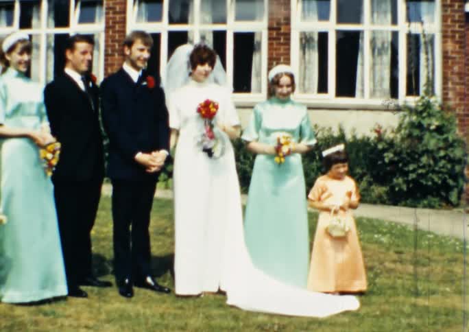 A bride and groom pose on the grass with the wedding party
