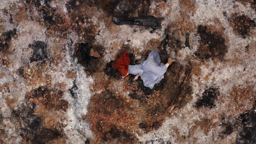 Young long haired redhead woman in a long blue dress laying over the moss in the ground