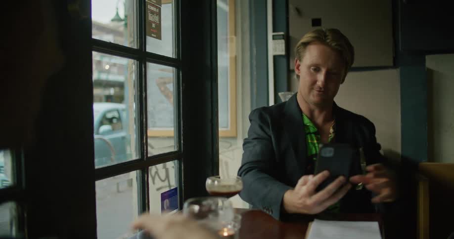 A person handing his cellphone to another man in a bar while they are talking