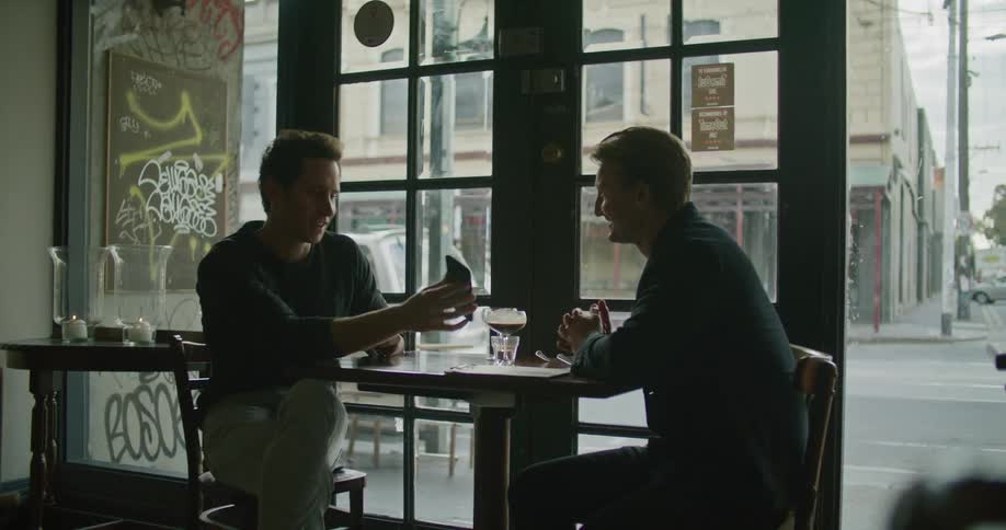 Young man sitting in a caf shows a friend something in his smartphone