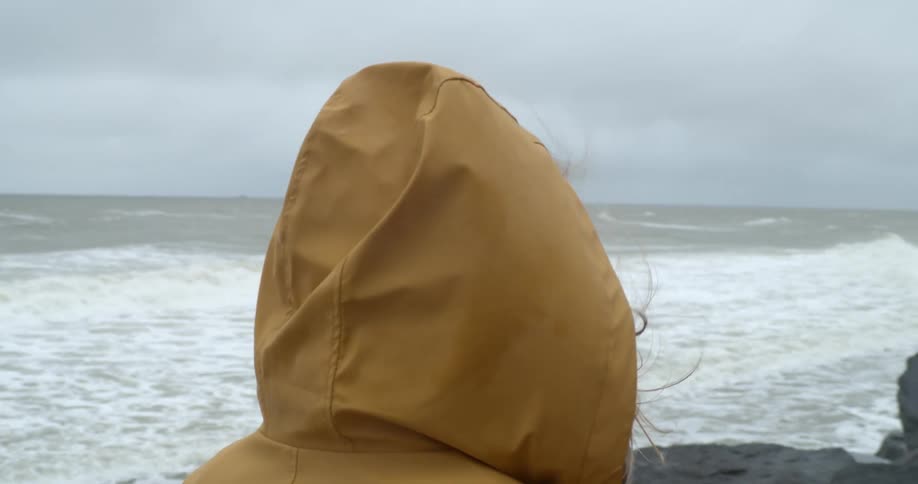 Woman wearing jacket stands near shore on windy day