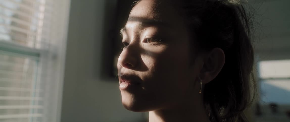 Sunlight shines through a window onto the face of a young woman who smiles as she gazes at something out of frame
