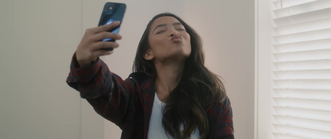A girl takes a selfie and laughs with a smartphone in a room at daytime