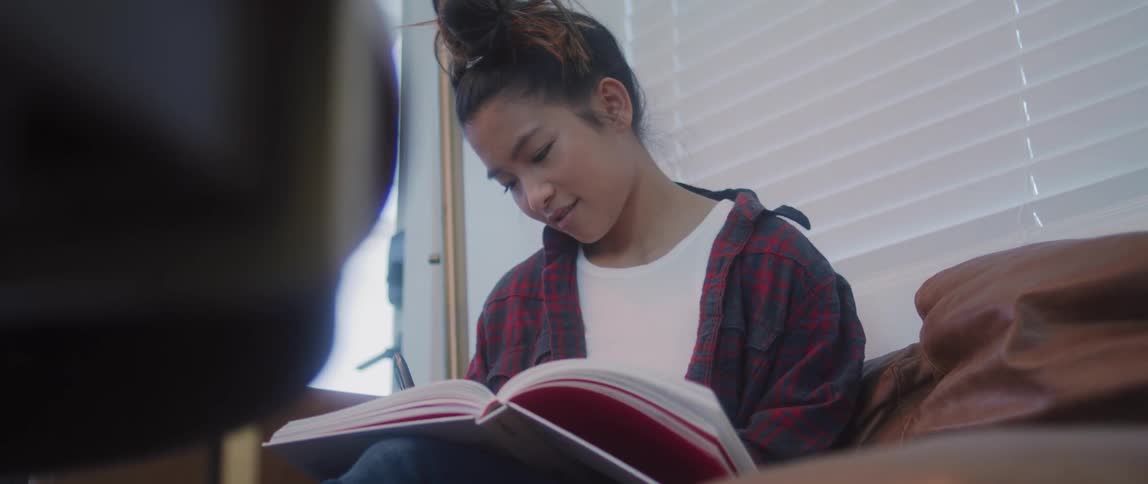 A teenage girl smiles as she writes in a book at home
