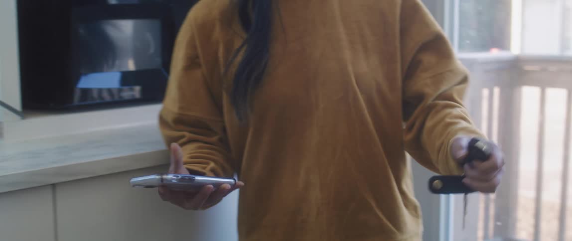 A young woman indoors puts on a facemask and then grabs her phone and keys and leaves the house