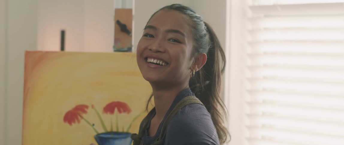 A female artist stands in front of her painting holding a paintbrush and laughing